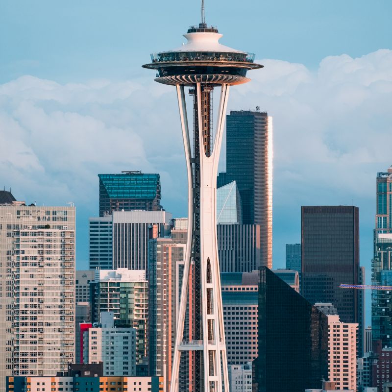 The image shows a city skyline with the Space Needle, surrounded by tall buildings and a partly cloudy sky in the background.