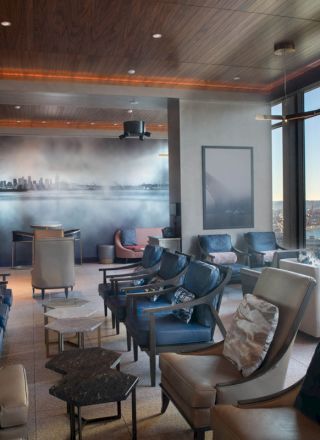 A modern lounge with plush seating, large windows overlooking city and water views, and dim lighting for a relaxed atmosphere.