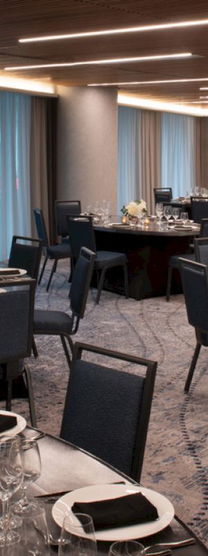 A banquet hall is set up with round tables, elegant tableware, and soft lighting, ready for an event or reception.