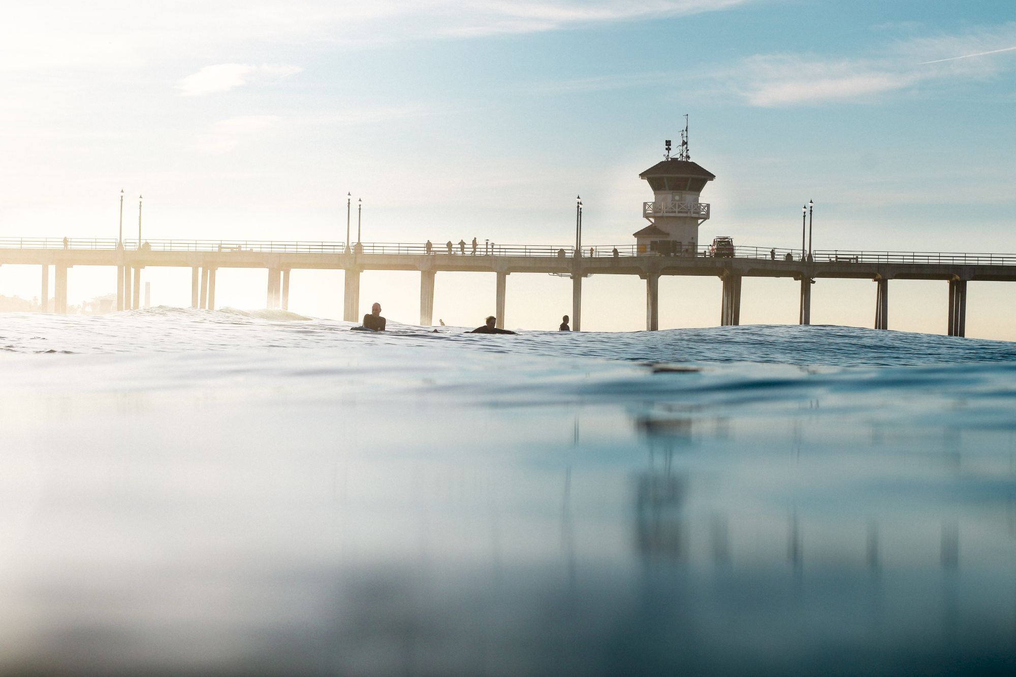 A serene view of a pier stretching into the ocean, with silhouettes of people and a lifeguard tower against a clear sky.